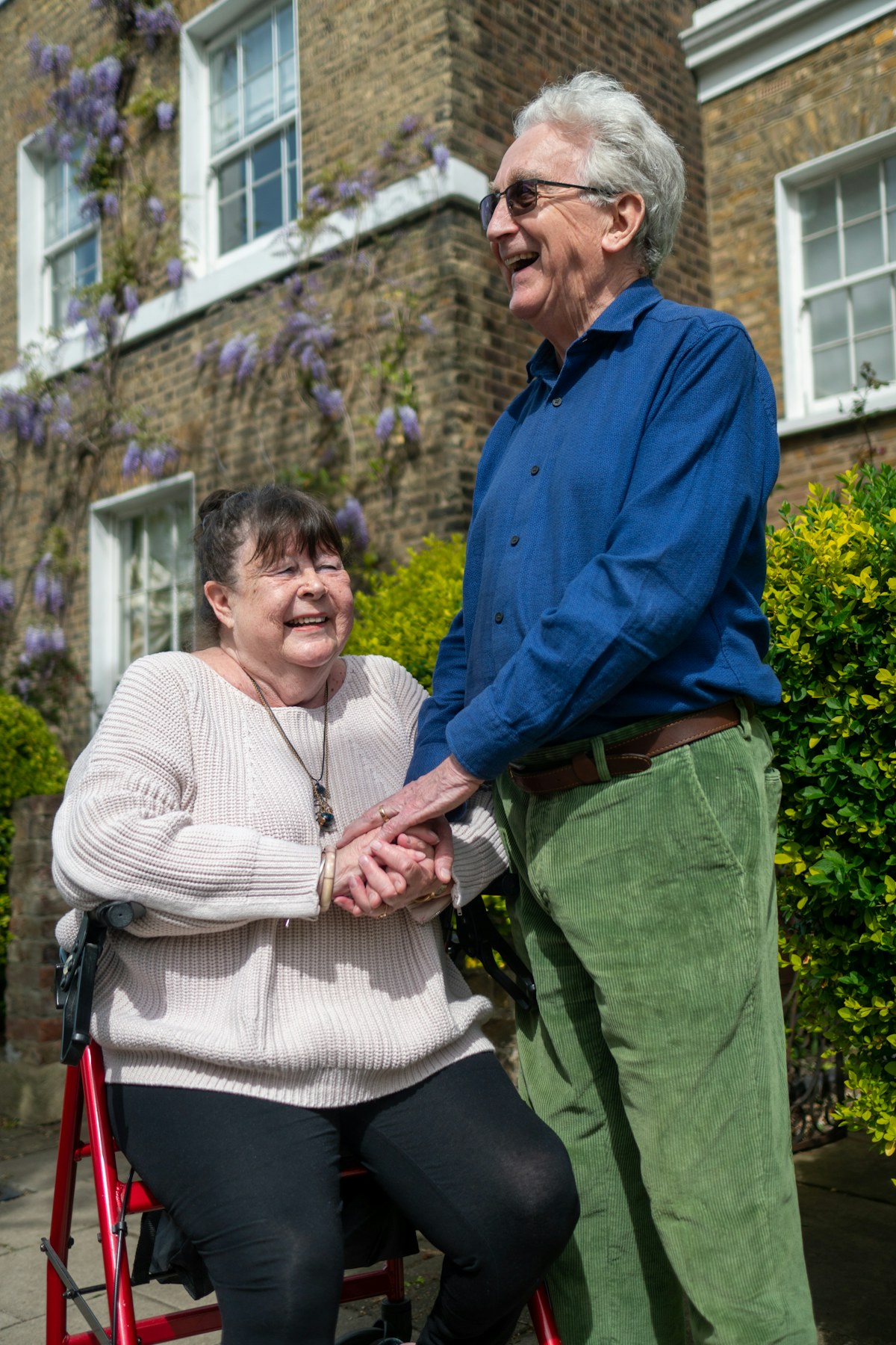 Two adults smiling together outdoors; one person uses a wheelchair